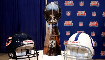 The Vince Lombardi Trophy sits between the Chicago Bears helmet on the left and the Indianapolis Colts helmet on the right on a table in front of an NFL backdrop