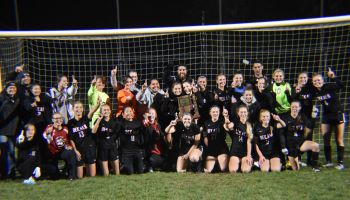 The DeKalb Girls Soccer team poses with their coaches in front of a soccer goal