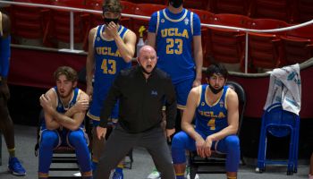UCLA Assistant Michael Lewis stands in front of the team bench with players behind him as he shouts orders to the guys in the floor