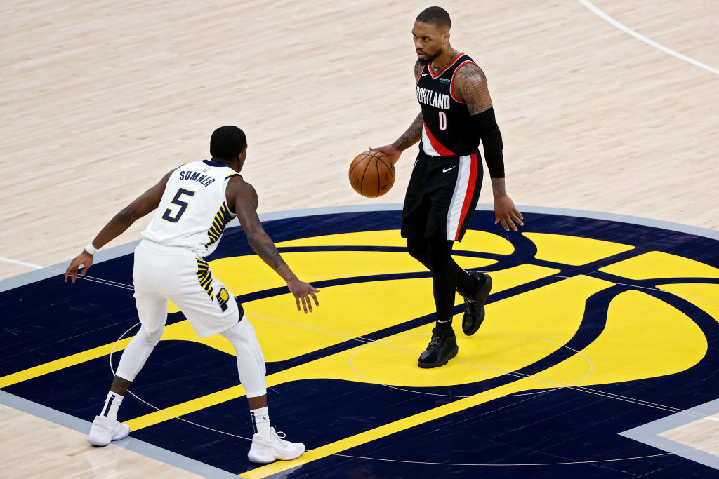 Damian Lillard dribbles the basketball on the Pacers logo at halfcourt closely defended by Edmond Sumner