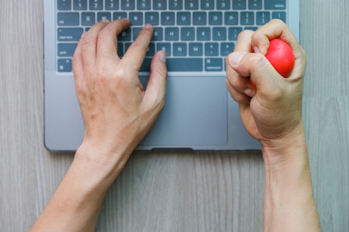 hand of a businessman who shows emotion squeezes a red ball with stress, anger, and aggression on the table with a laptop computer. health concept
