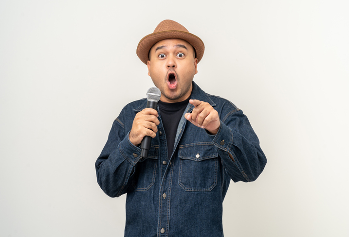 Shocked face young asian man singing song. Artist vocalist singer on isolated background. Confident man public speaking talking with microphone in studio.
