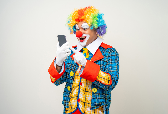 Mr Clown. Portrait of Funny face Clown man in colorful uniform standing holding smartphone. Happy expression male bozo in various pose with cellphone on isolated background.