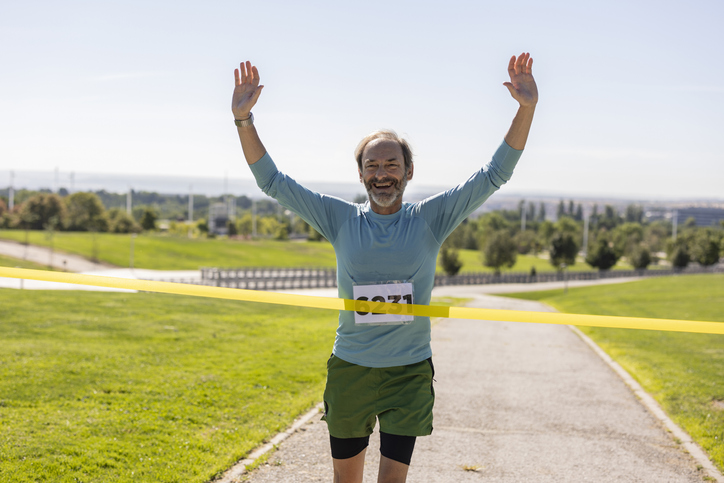 Happy senior running across the finish line - Mature man running marathon race. -