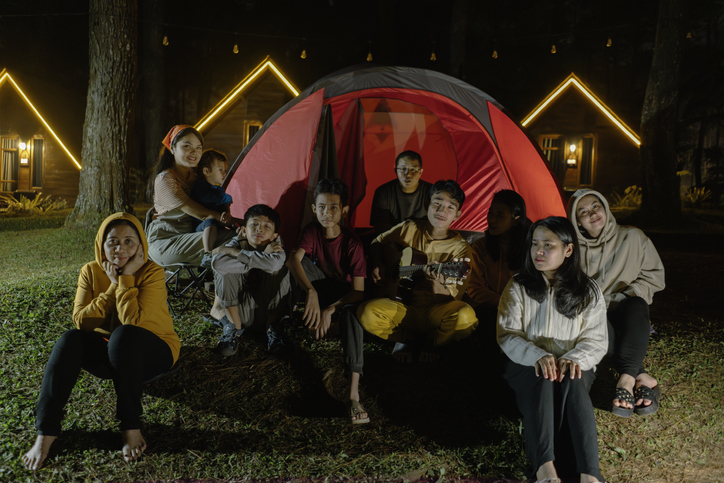 Group of family having fun playing guitar while camping at the night