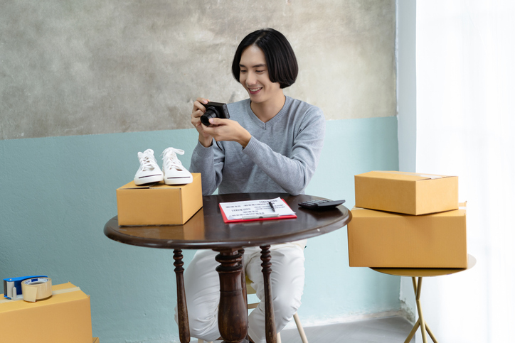 Young freelance Asian man seller taking photo to shoes with digital camera for post to sell online on the internet or marketing socail media.Start up small business owner,Selling online ideas Concept.