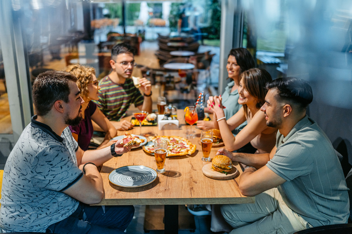 Group Of Friends Drinking And Eating Burgers And Pizza In A Bar Indoors