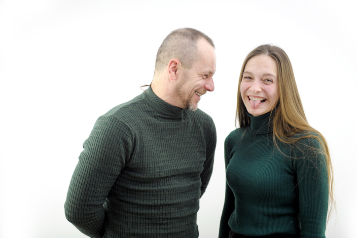 a girl trolls a man a young girl with long hair shows her tongue to him father and young daughter smile joy fun good mood couple in dark green stockings smiles the joke is perceived