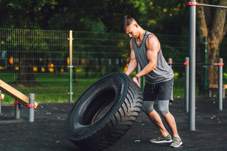 Tire flipping workout: bodybuilder pulls and flips tractor tire during workout in the park.