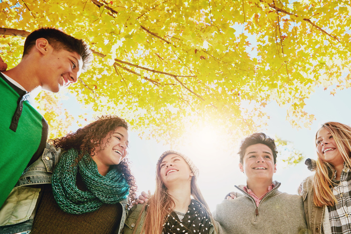Tree, happy and group of friends in park for outdoor adventure, bonding and vacation together. Low angle, sky and people with smile in nature for friendship, support and break on holiday in Manhattan