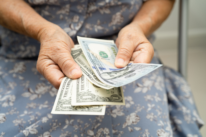 Asian senior woman holding and counting US dollar banknotes money in purse. Poverty, saving problem in retirement.