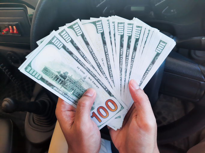hand holds cash dollars on the background of the steering wheel of a car. Concept of car sale, purchase and leasing.