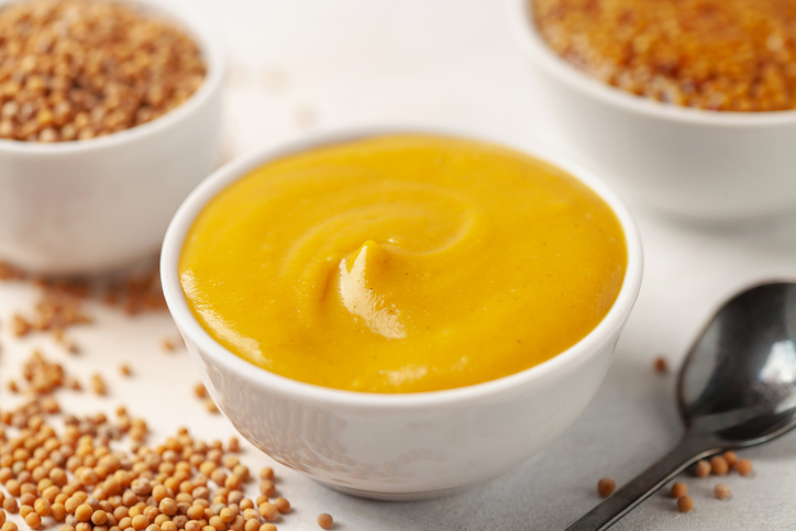 Mustard sauce in a bowl and seeds on a bright background.