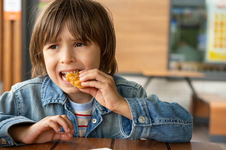 Little boy is eating chicken nuggets in fast food Restaurant or cafe.