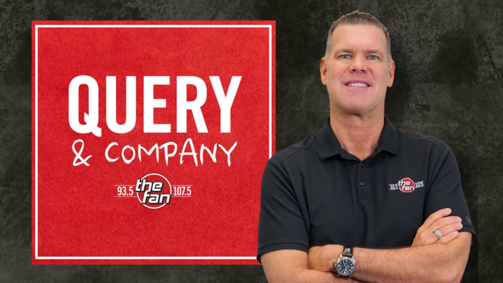 A man with short gray hair wearing a black polo shirt standing in front of a large red sign that says "QUERY & COMPANY 93.5 the fan 107.5".
