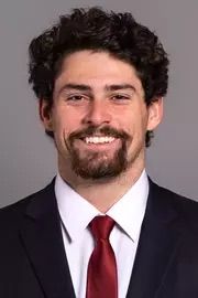 Headshot of a smiling man with curly dark hair wearing a suit and red tie.
