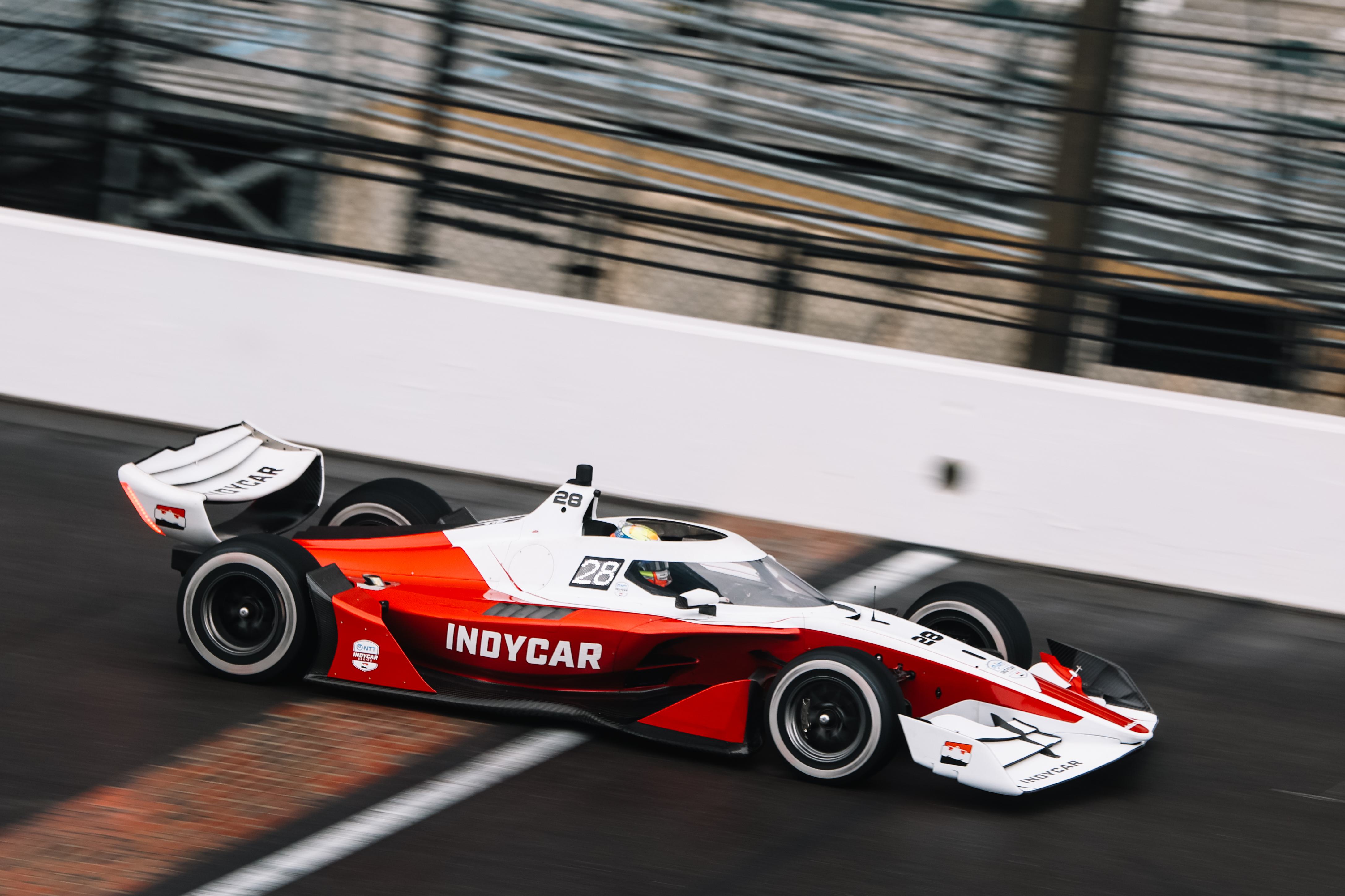 A high-speed IndyCar race car in motion, with the "IndyCar" logo clearly visible on the side of the vehicle.